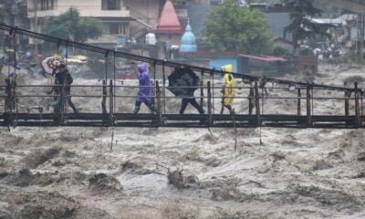 People walk through a bridge across River Beas swollen due to heavy rains in Kullu District, Himachal Pradesh