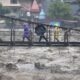 People walk through a bridge across River Beas swollen due to heavy rains in Kullu District, Himachal Pradesh